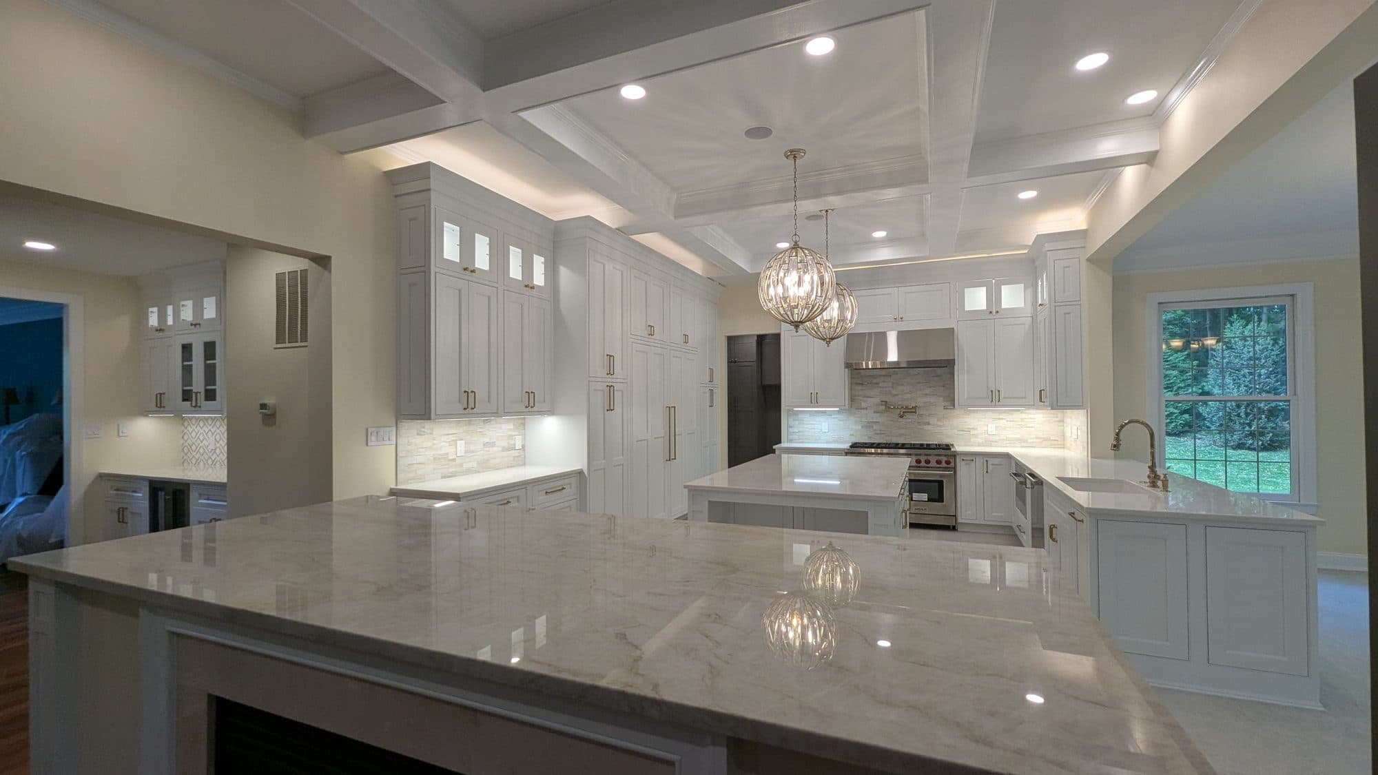 Wide view of a renovated kitchen with a large island, pendant lighting, and shaker cabinetry