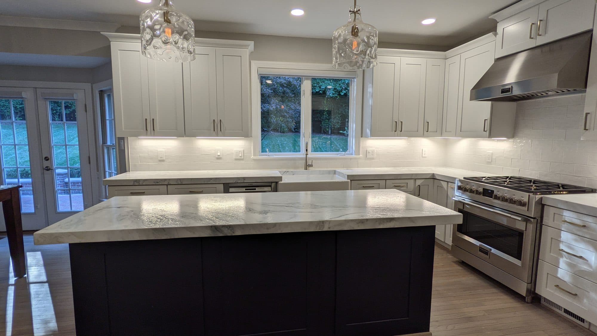 Kitchen with a navy island, waterfall marble countertop, farmhouse sink, and professional-style gas range
